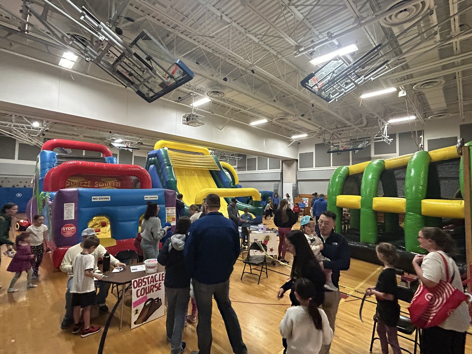 Families enjoying a busy indoor school carnival with inflatable attractions